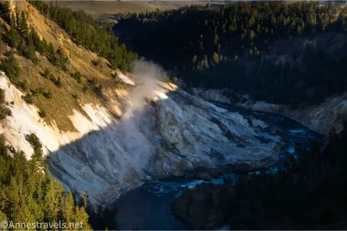 A river winds below a white hillside steaming with geothermal springs