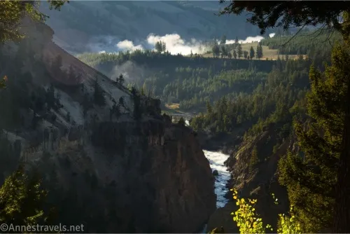 A river twists through a forested canyon with clouds rising over the hill 