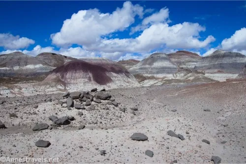 Puffy white clouds over colorful badlands and rocks on a desert plain