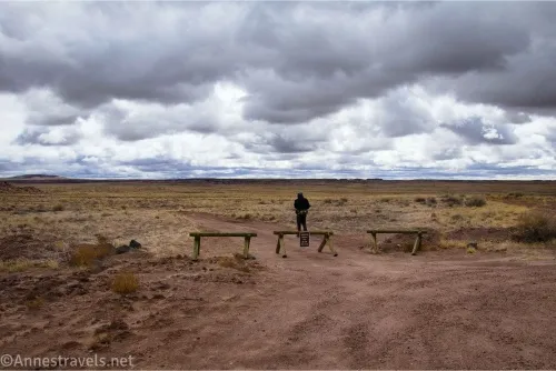 Dark clouds over a desert plain with three fence pieces and a hiker on a dirt road