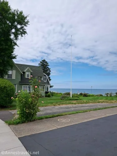 Sidewalk between two driveways with a rosebush and a flagpole with Lake Ontario in the background 