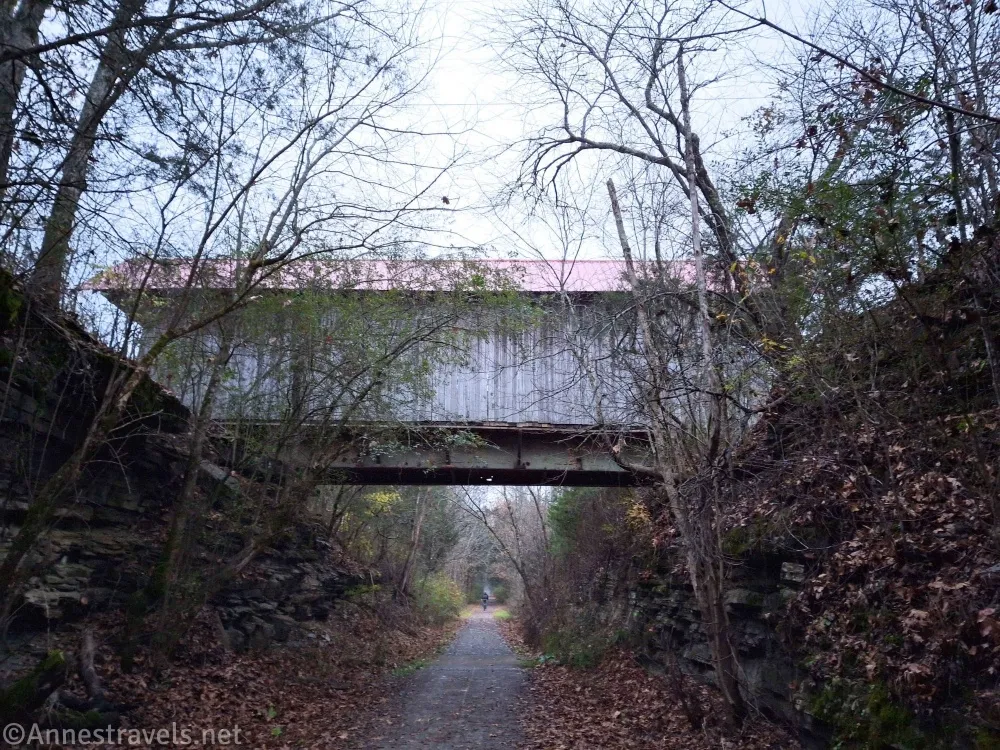A covered bridge over a gravel path surrounded by trees