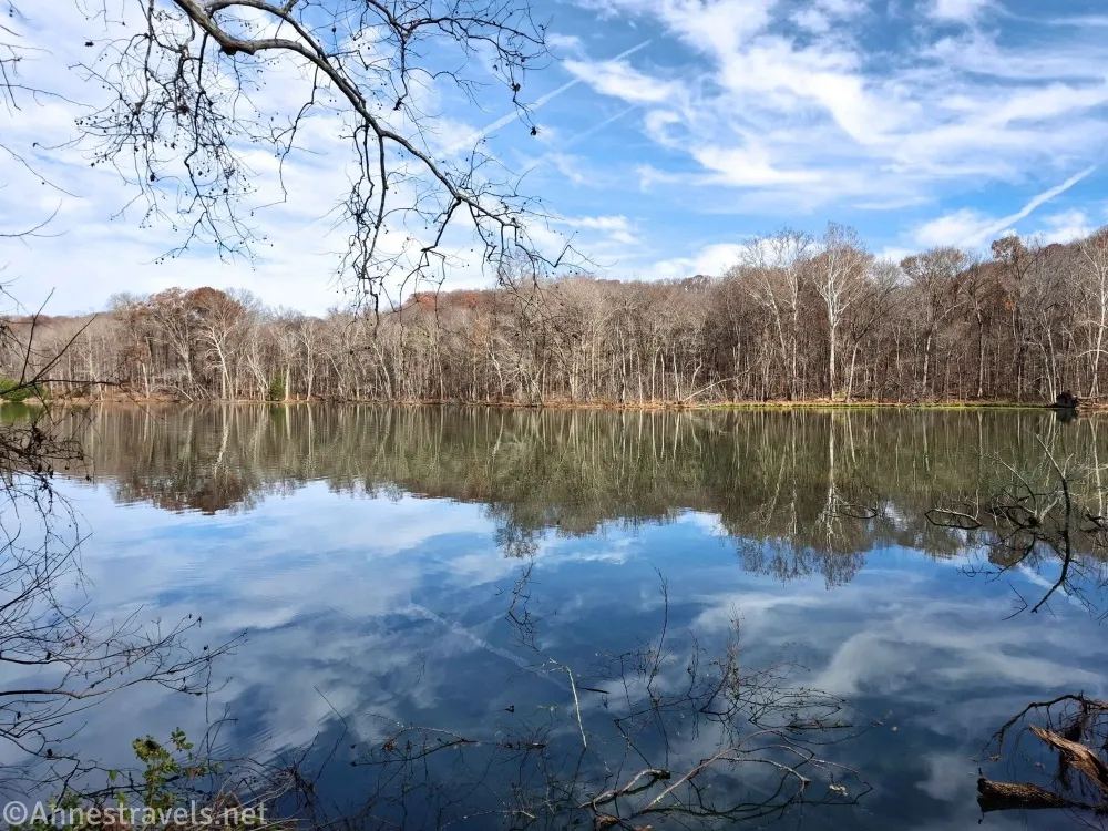 A lake reflects the trees on the shoreline and clouds in the sky