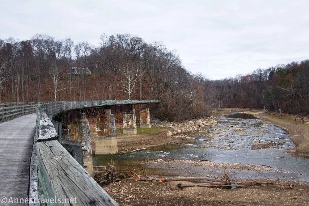 A bridge on concrete piers crosses a river with leafless trees beyond