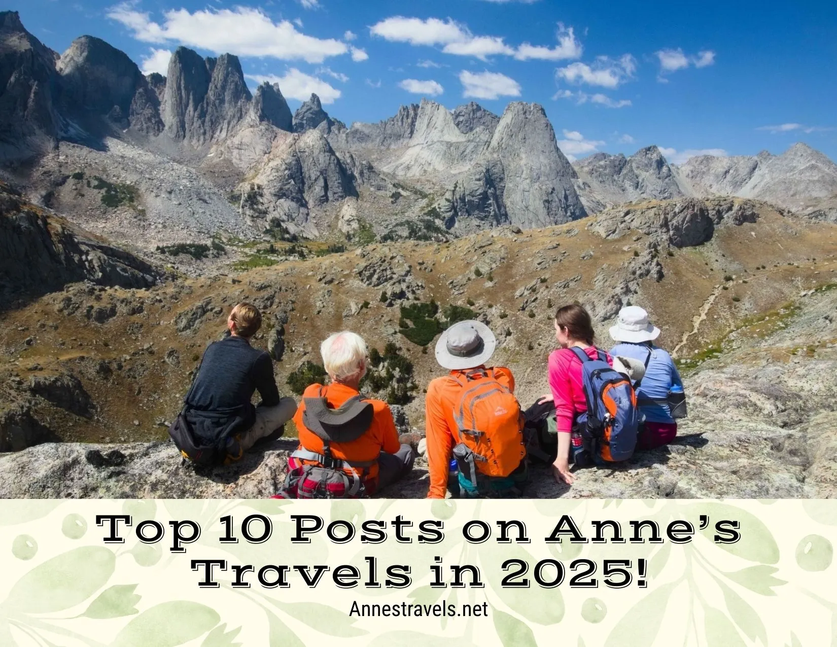 Five hikers in gray, orange, pink, and blue shirts look at the scenery of rugged mountains with clouds in the blue sky 