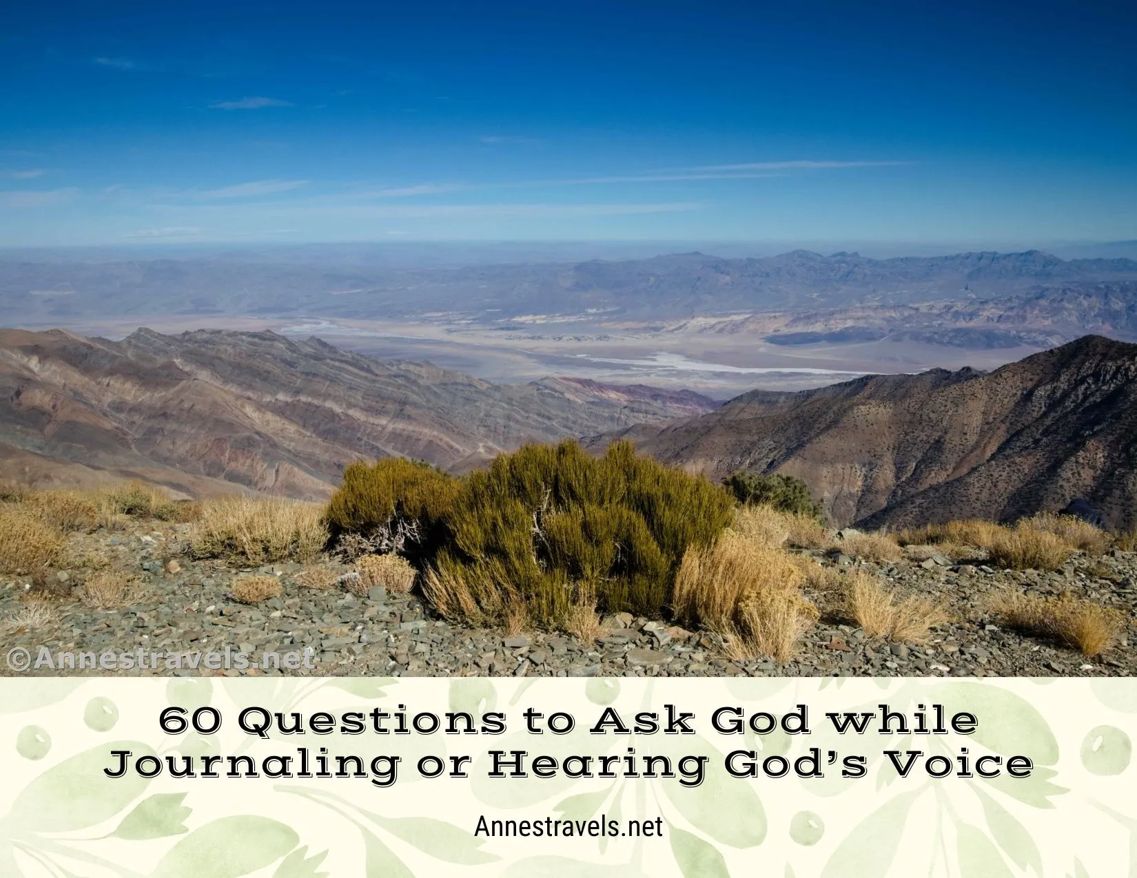 A rugged desert landscape with bushes close and striped badlands and a valley and mountains further away 