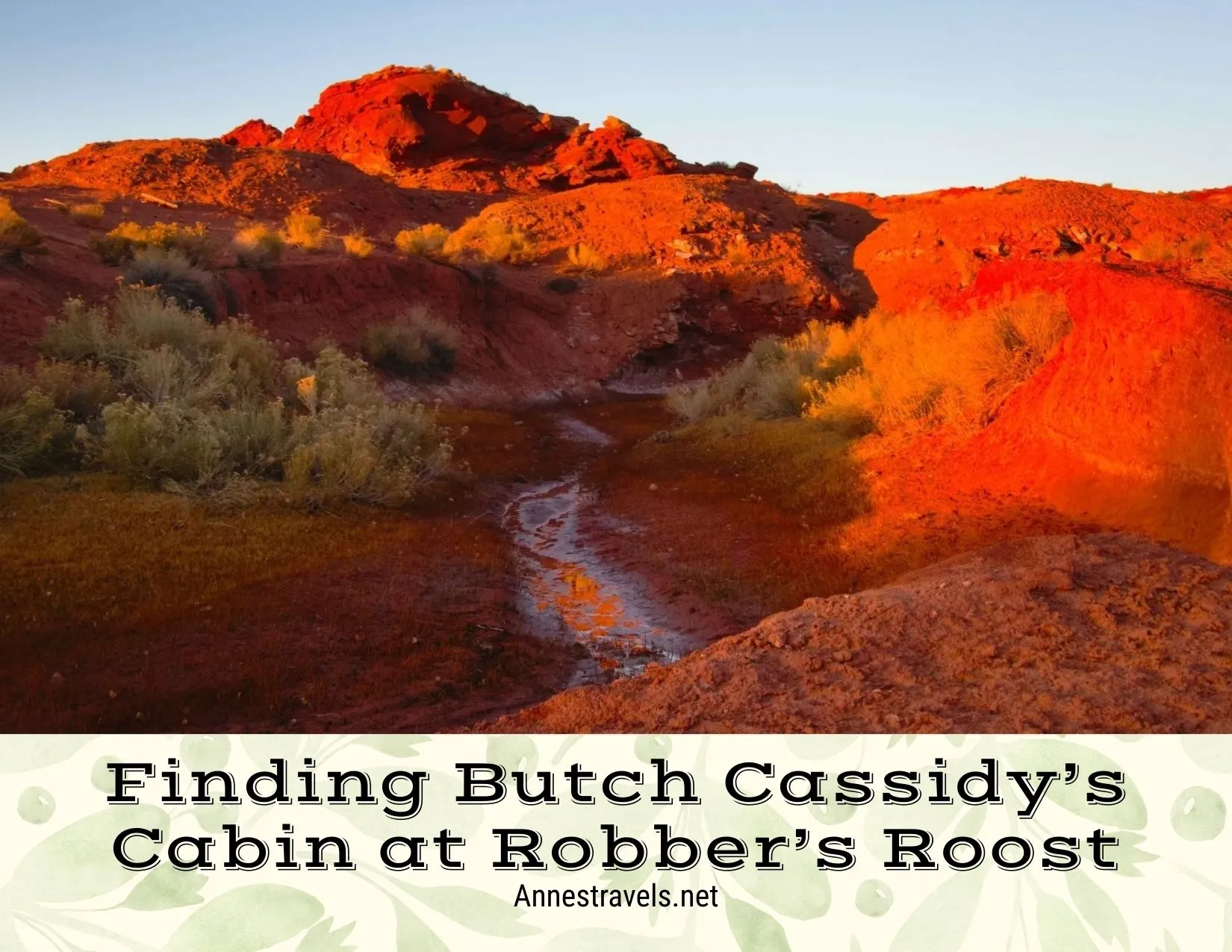 A stream runs below red rocks and a red hill 