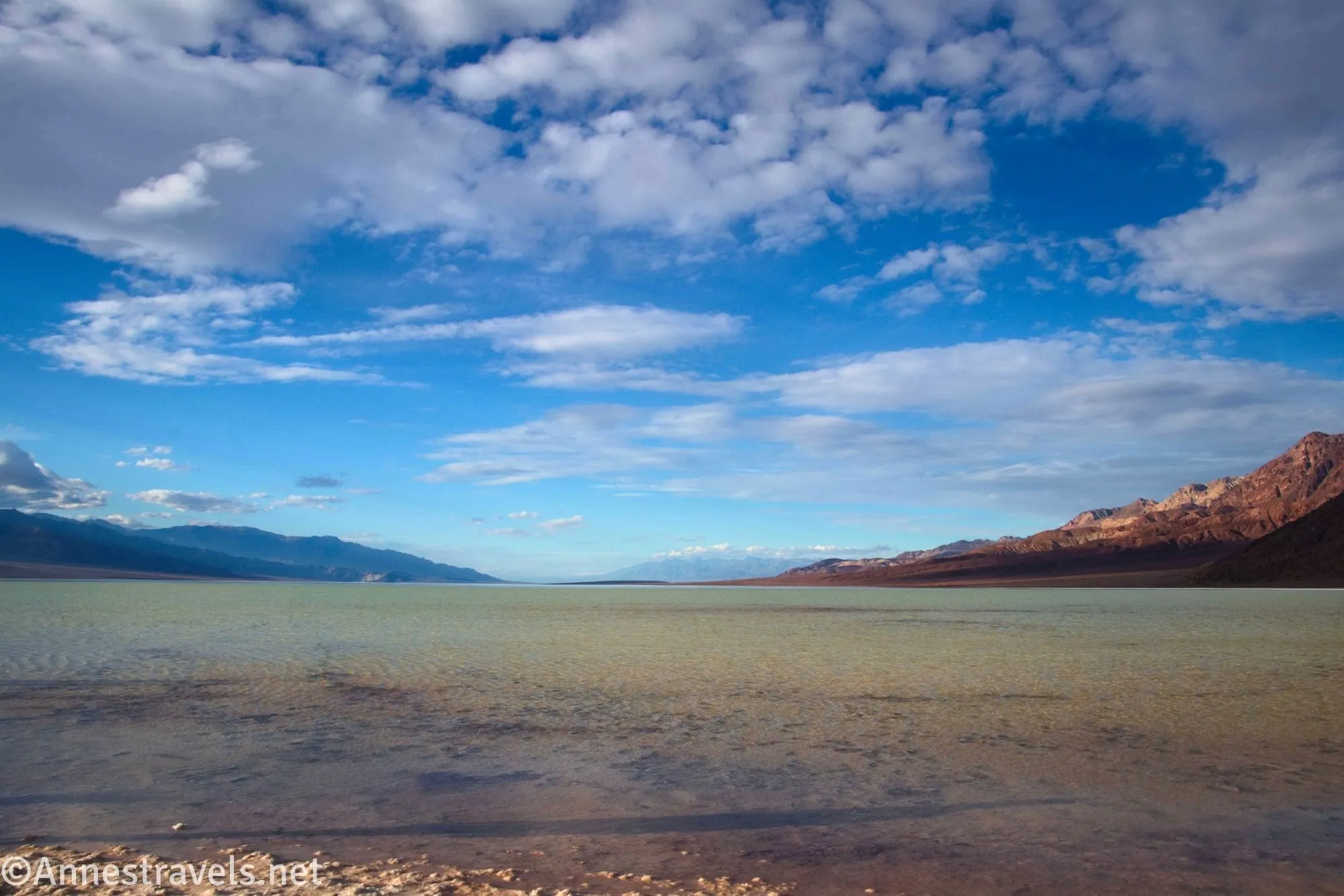 A desert lake between mountains and below clouds in a blue sky