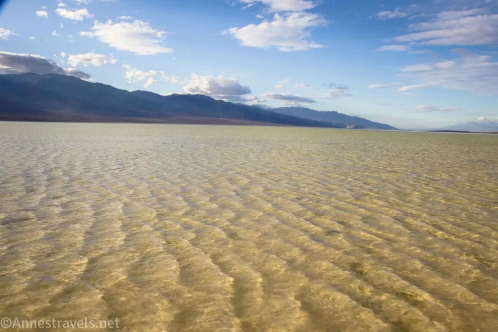 Ripples on a shallow desert lake with distant mountains and clouds in a blue sky