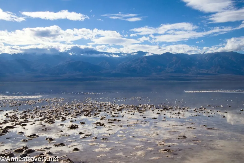 Salt formations and reflections in a lake with distant mountains and clouds