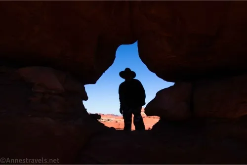 Silhouette of a man in an arch with red rocks and blue sky behind him