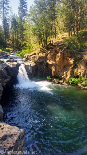 A waterfall and a green pool below yellow cliffs and green trees 