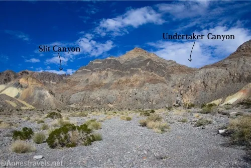 Arrows and text marking Slit Canyon on the left and Undertaker Canyon on the right in colorful desert mountains above a gravelly wash 
