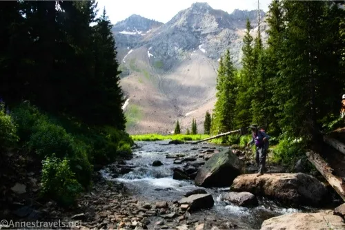 Mountains in the background of a stream in a forest with a hiker looking at the stream