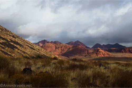 Red hills across a desert plain beneath gray and white clouds 