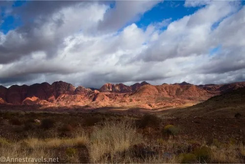 Clouds sail above red hills in the distance and shadow the nearby plain