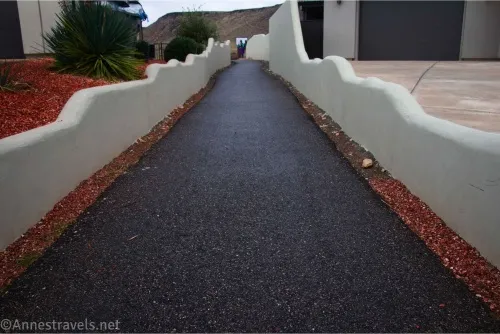 A blacktop sidewalk between white walls and bordered by red gravel
