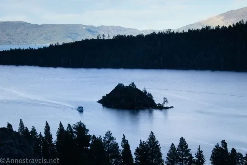 A shadowy island in a lake with shadowy trees on the banks and a boat near the island