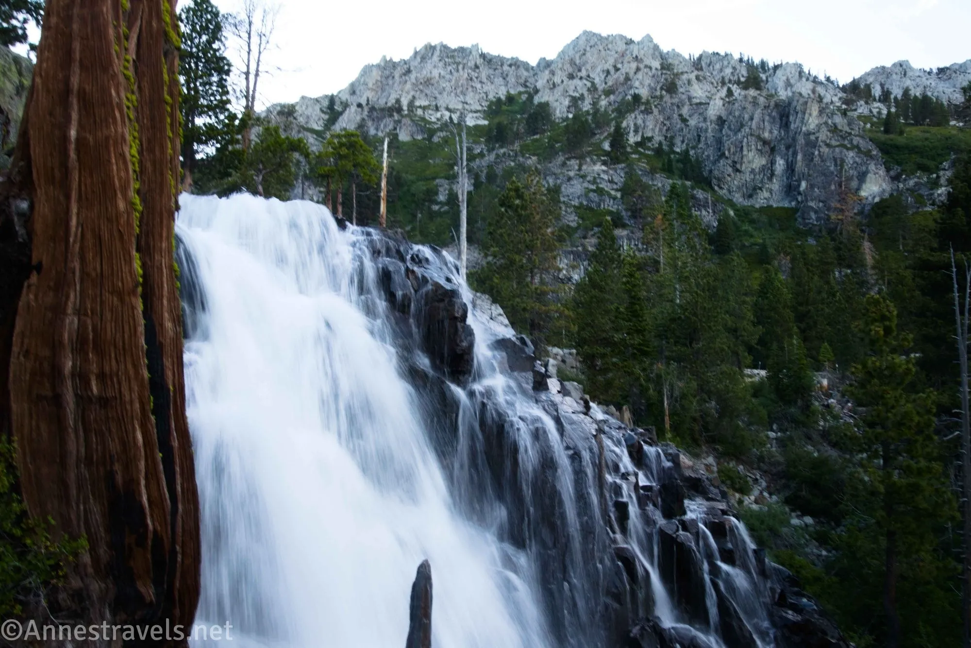 A waterfall tumbles down a rocky cliff face with trees and cliffs beyond