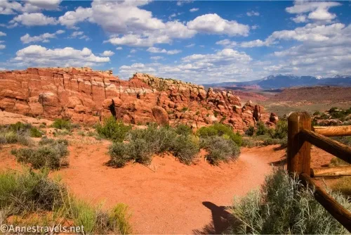 Rock formations and desert scrub and a fence under clouds in a blue sky