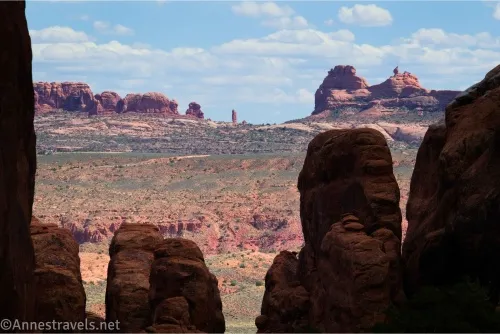 Shadowy rock spires in the foreground, a sunny desert plain, and distant rock formations