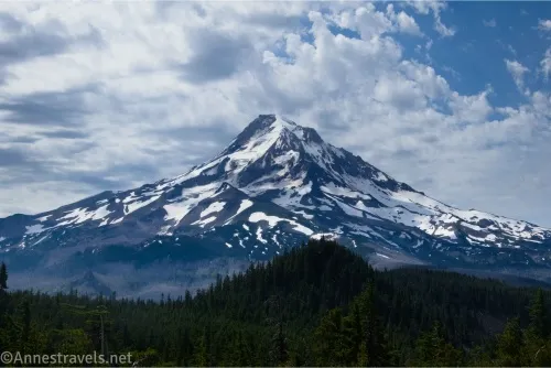 Dramatic clouds over a snowy volcano with a dark hill in the foreground 