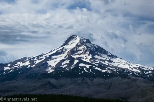 Dramatic clouds behind a snowy volcano with a gray foreground 