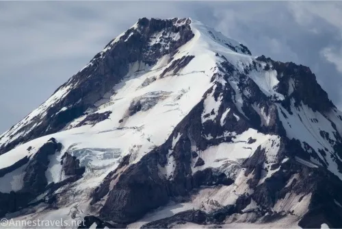 The snowy and rocky peak of a volcano with clouds in the background