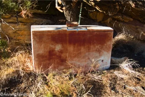 A rusty freezer with a rock on top of it in dry yellow grass