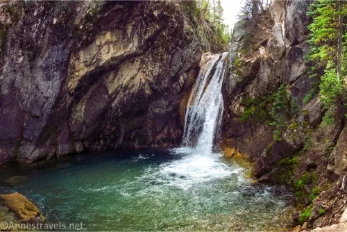 A waterfall tumbles between rocks into a green pool