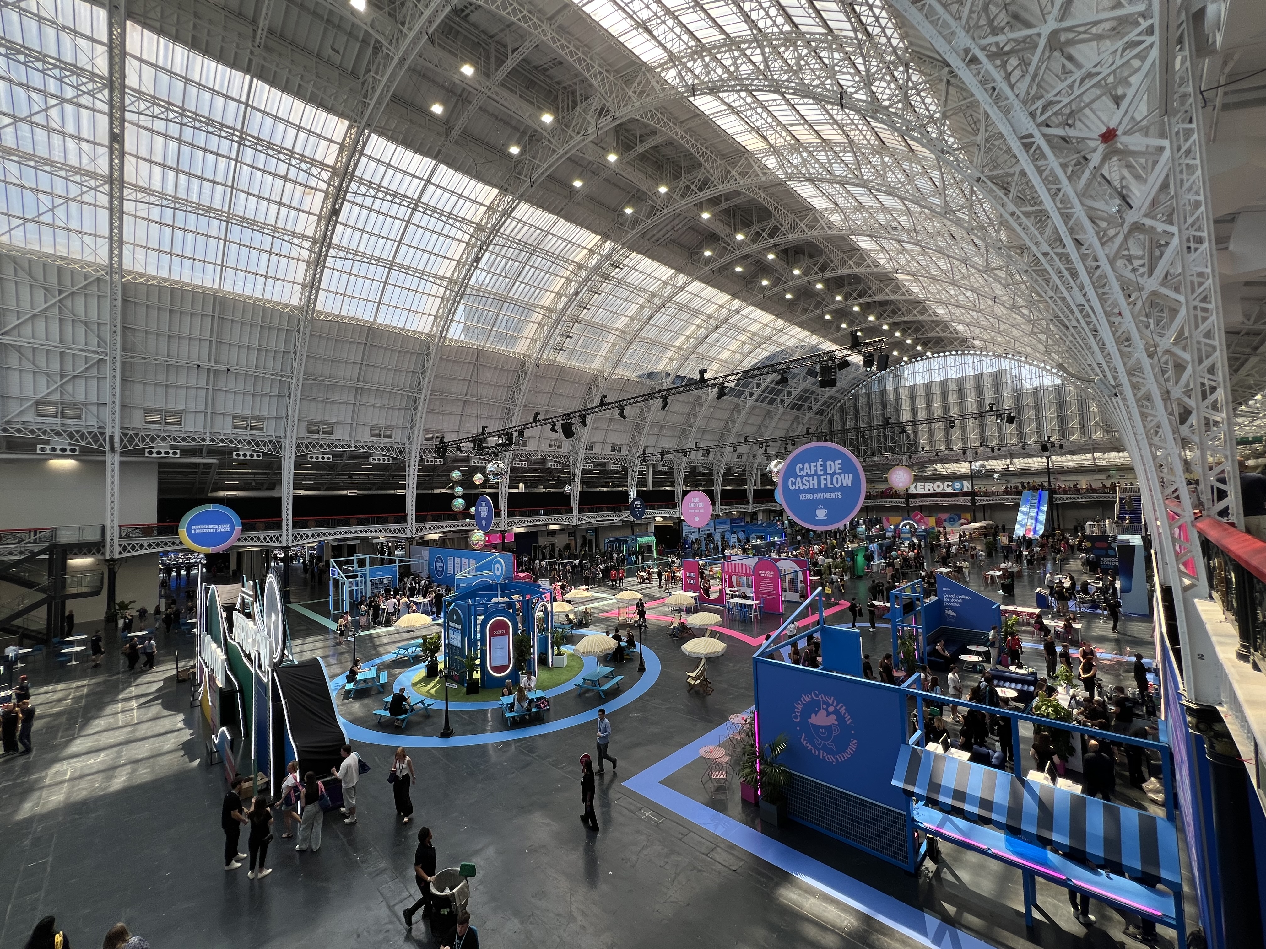 The Xerocon London 2026 show floor at Olympia, with the Cafe de Cash Flow stand and delegates milling between activations under the glass roof
