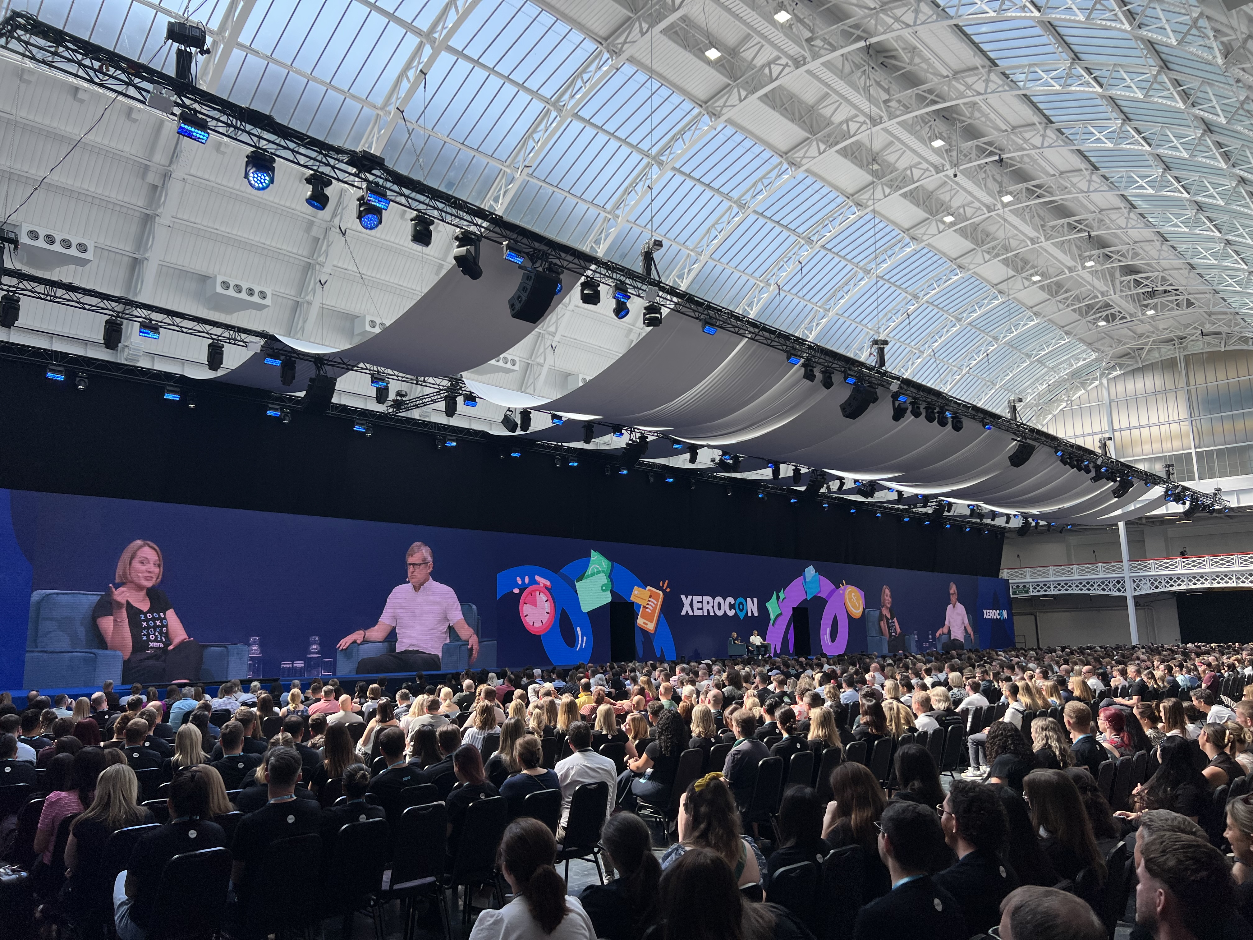 The Xerocon main stage keynote, with two speakers seated on screen above a packed auditorium