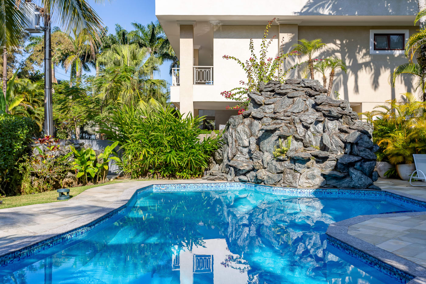 Piscina com cascata de pedra e jardim tropical