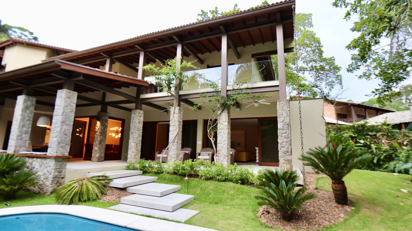 Fachada com pilares de pedra natural e jardim tropical
