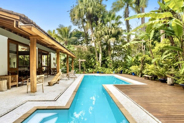 Piscina em L com deck de madeira e jardim tropical