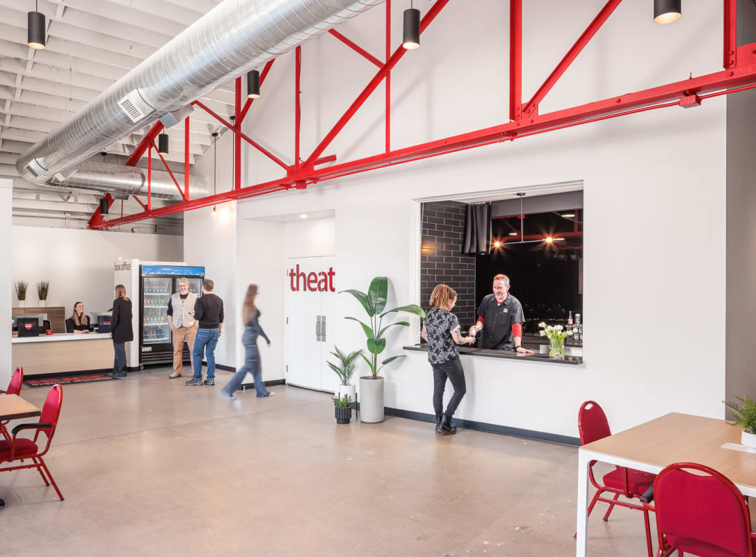 An interior view of the HUGE Improv entry vestibule, box office desk, concessions, and theater entrance with pops of red accents throughout in the chairs and overhead supports.