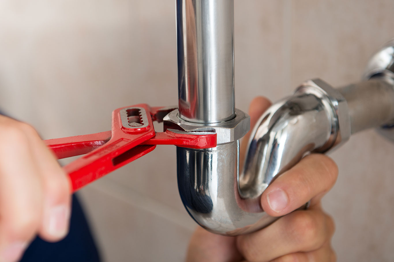 a coldstream mechanical plumber’s hands hold a sink pipe gripped in a pipe wrench as he installs plumbing fixtures in new vernon bc home