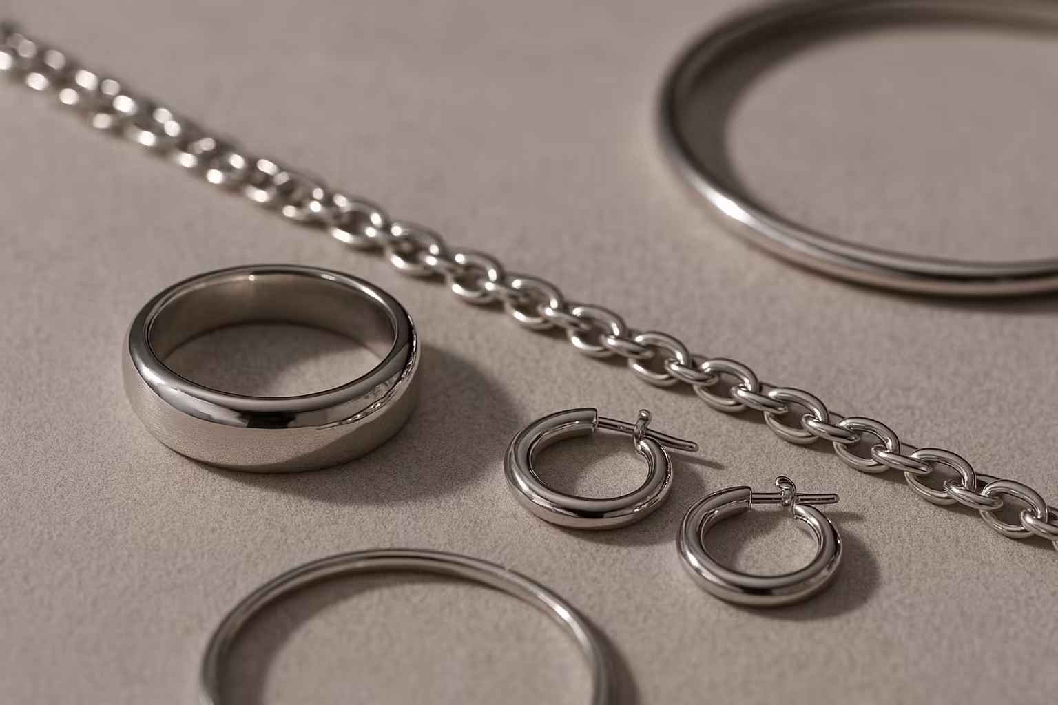 Collection of silver jewelry pieces on neutral background showing rings, necklaces and bracelets with focus on finish and details