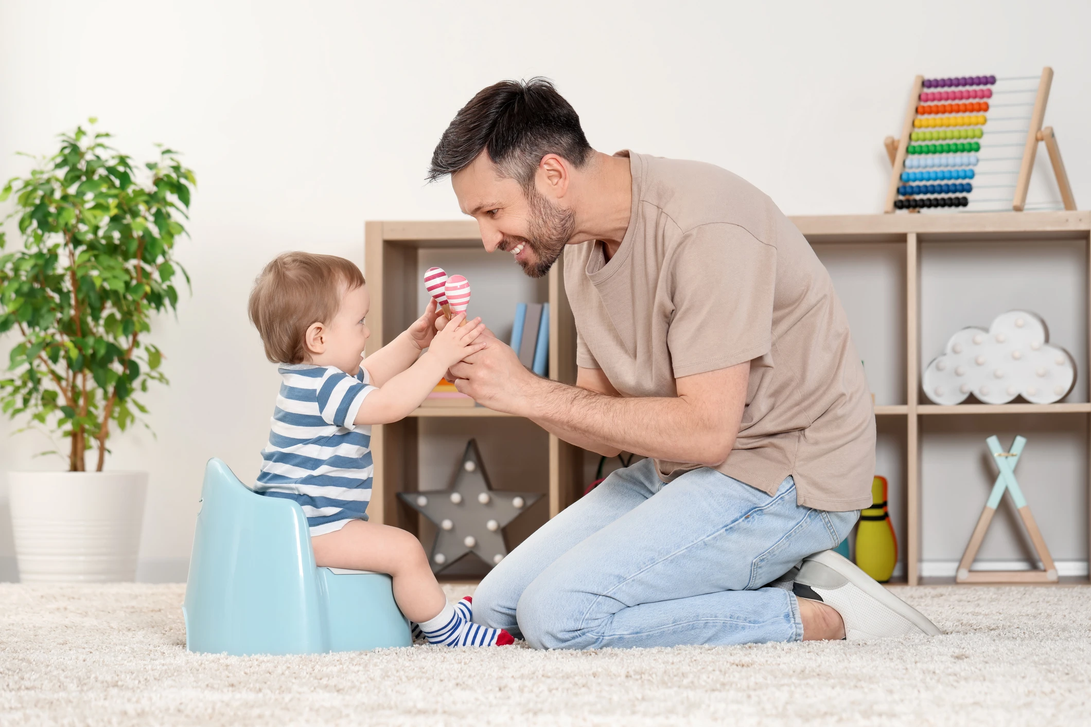 Father training his child to sit on baby potty indoors