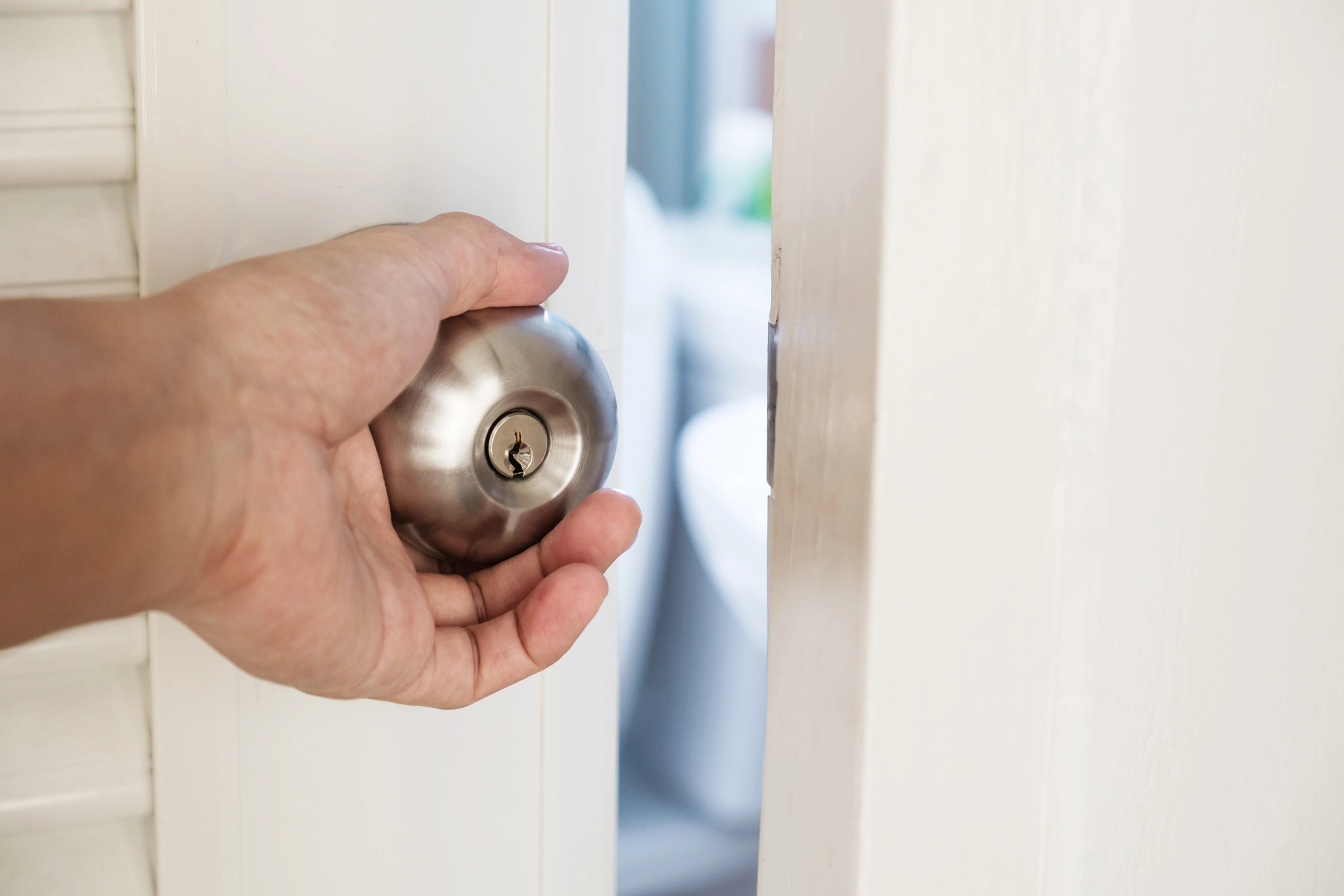 Close-up hand holding door knob, opening door slightly, selective focus