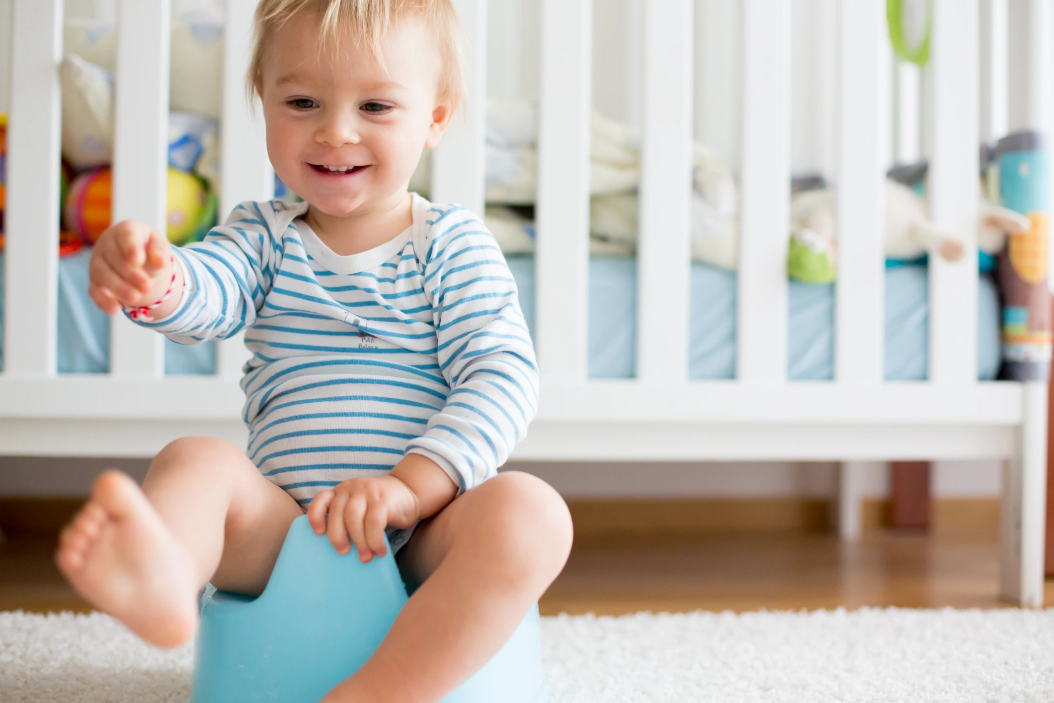 Cute toddler boy, potty training, playing with his teddy bear on potty