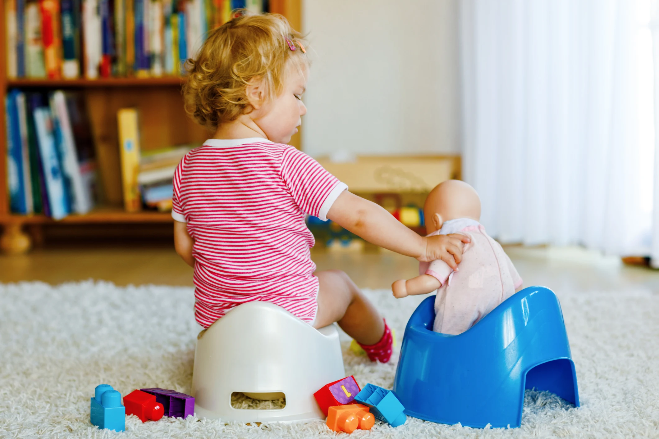 Closeup of cute little 12 months old toddler baby girl child sitting on potty. Kid playing with doll toy. Toilet training concept. Baby learning, development steps.