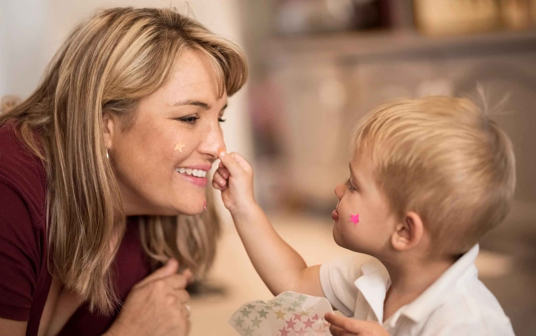 Shot of little boy placing star stickers on mother's face at home