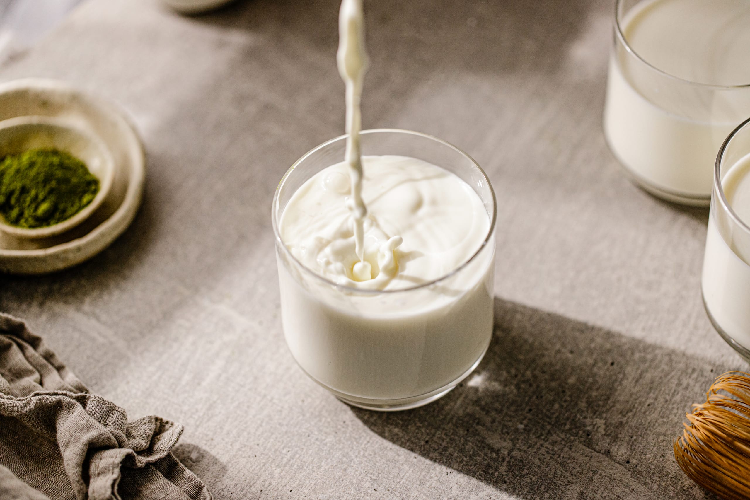 Close-up of pouring fresh milk in glass. Milk is being poured in a glass on the kitchen table at home.