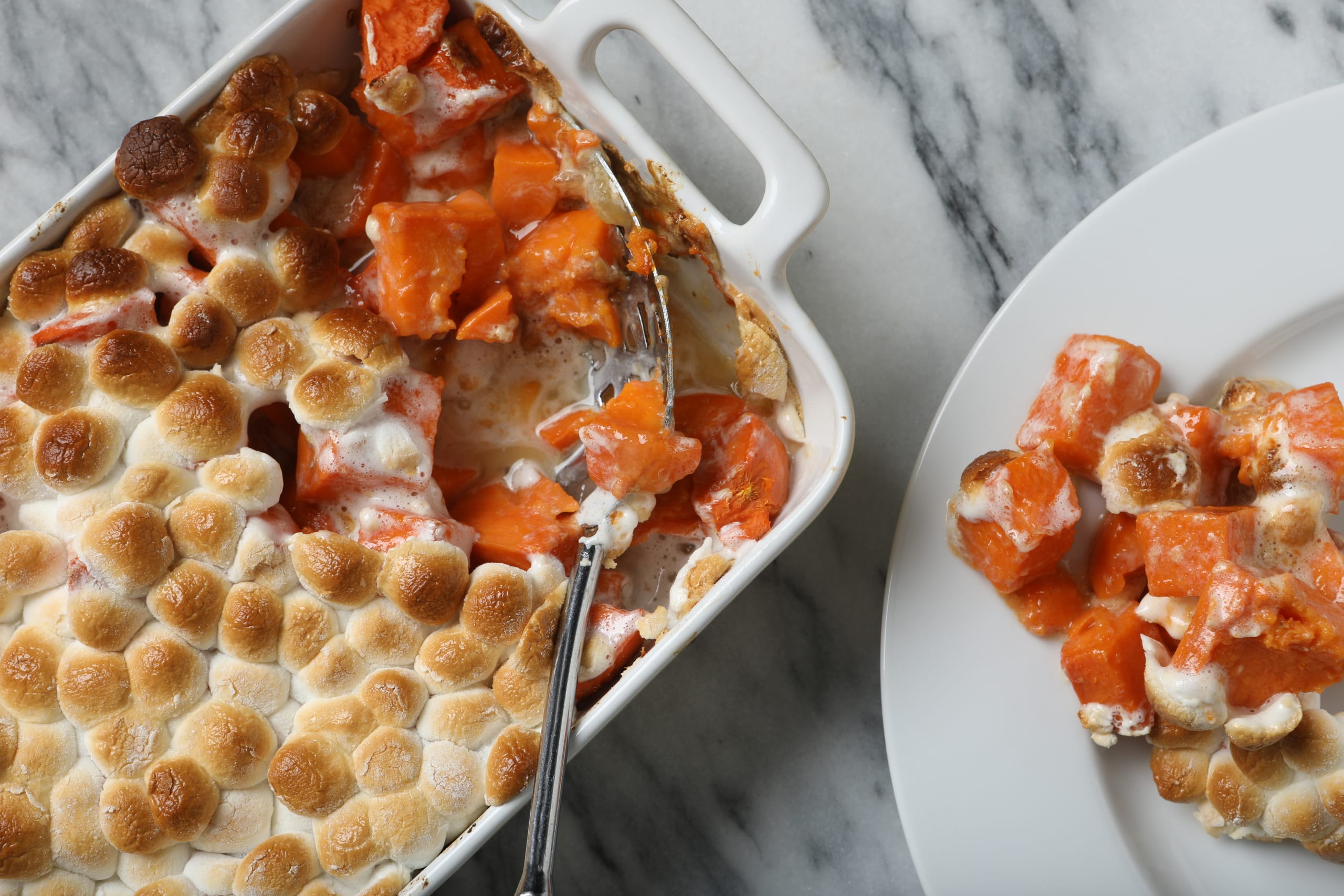 An overhead extreme close up horizontal photograph of a Thanksgiving sweet potato casserole dish and a serving of the potatoes on a white plate.