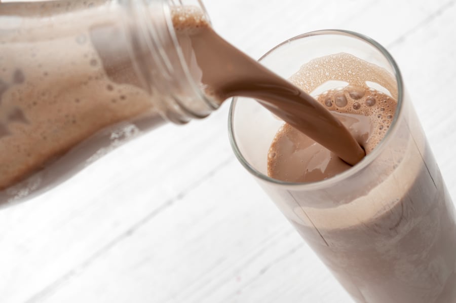 bottle pouring chocolate milk into a tall glass isolated on rustic white wood background