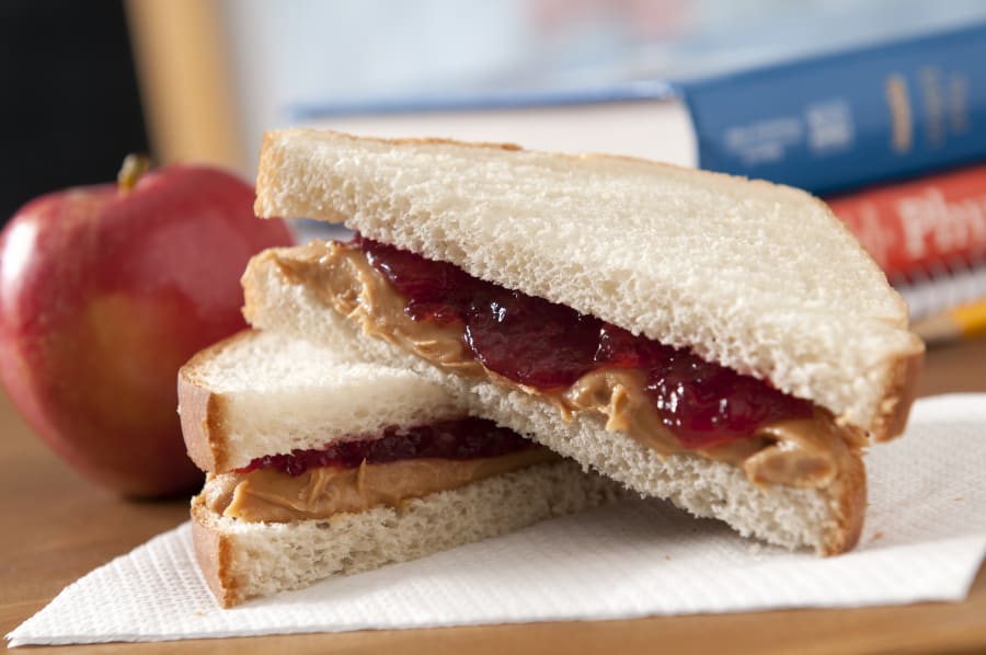 Peanut butter and jelly sandwich with a apple in a classroom.