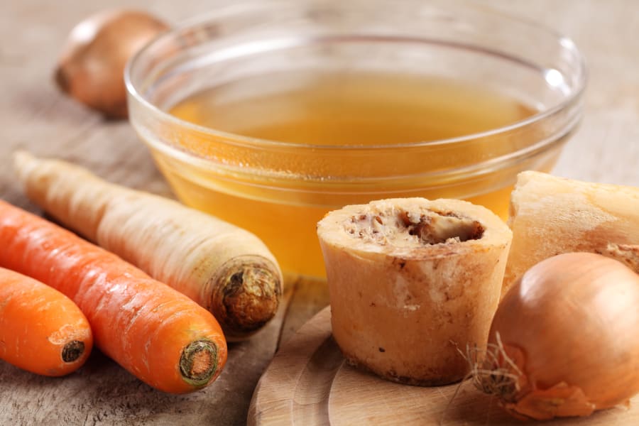 Bowl with beef broth, boiled bones and fresh vegetables.