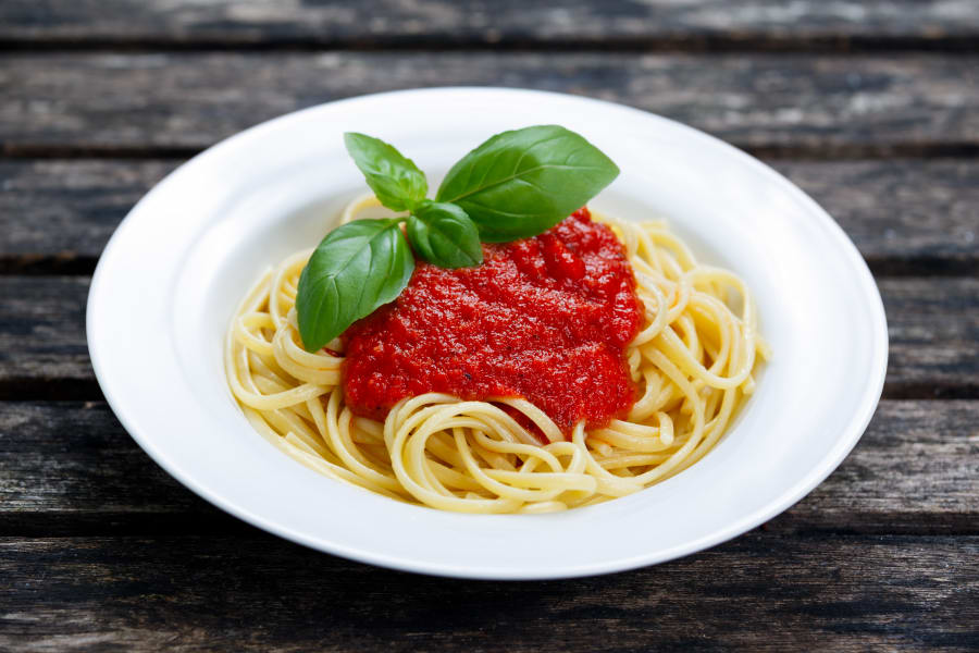 Spaghetti with marinara sauce and basil leaves on top, on wooden table