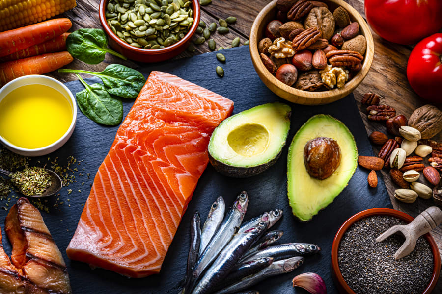 high angle view of salmon, sardines, avocado, extra virgin olive oil, and various nuts and seeds like pumpkin seeds, chis seeds, pecan, almonds, pistachio, walnuts and hazelnuts.